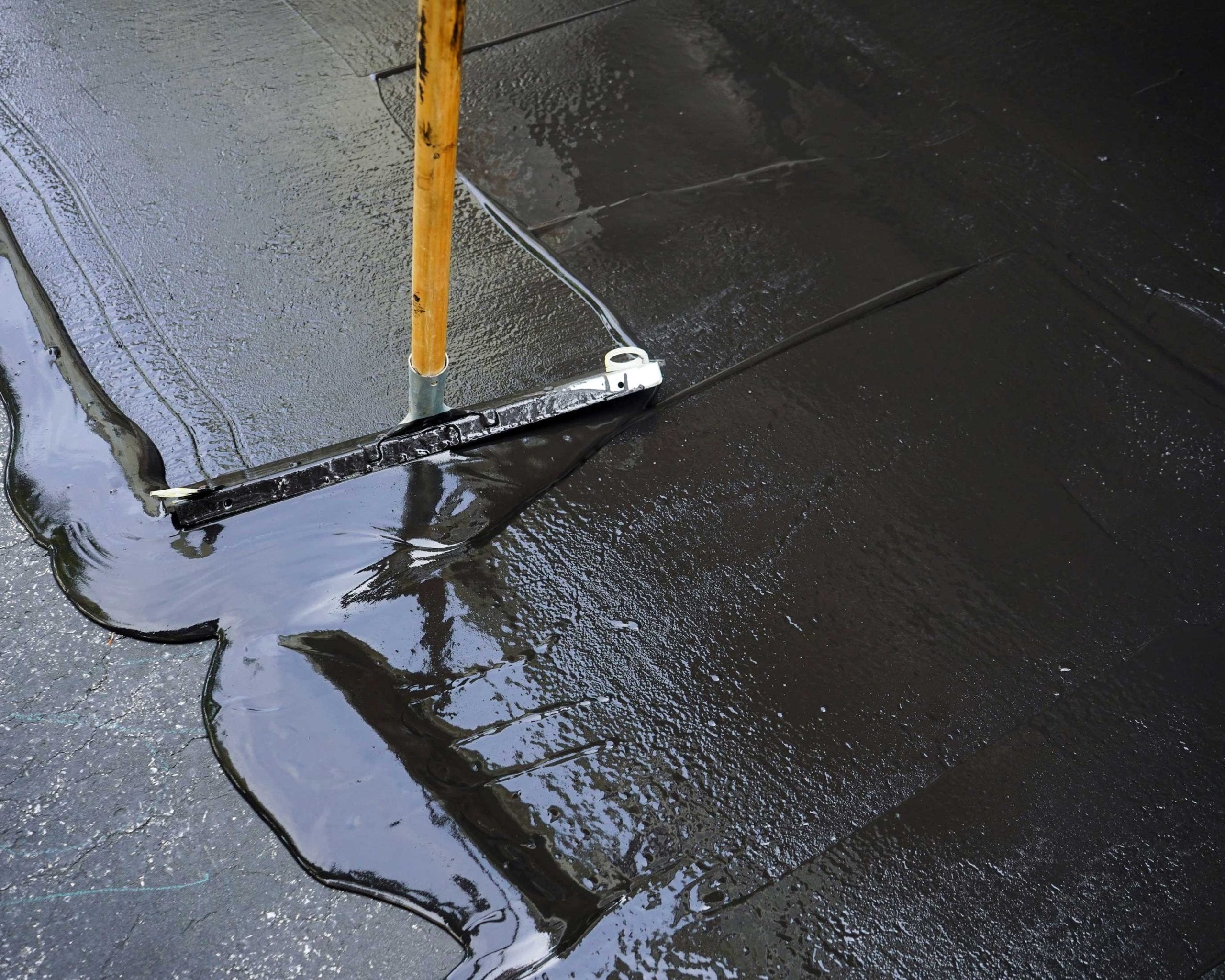 An asphalt contractor uses a squeegee to sealcoat a driveway.